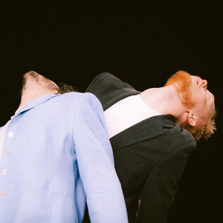 Two men in stylish suits tilt their heads back. The man on the left has a light jacket, while the other is wearing a dark one. | © Viktor Sorma