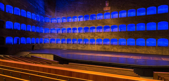 Un teatro elegante con accenti di luce blu. Le file di sedili sono vuote e l'area del palco è chiaramente visibile. | © Andreas Kolarik