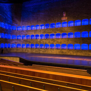 A stylish theater with blue light accents. The rows of seats are empty and the stage area is clearly visible. | © Andreas Kolarik